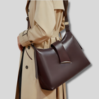 Sac bandoulière en cuir marron porté à l’épaule sur trench beige, style urbain chic et intemporel.