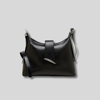 Sac bandoulière en cuir noir, forme souple minimaliste, bandoulière réglable et détail métallique signature.